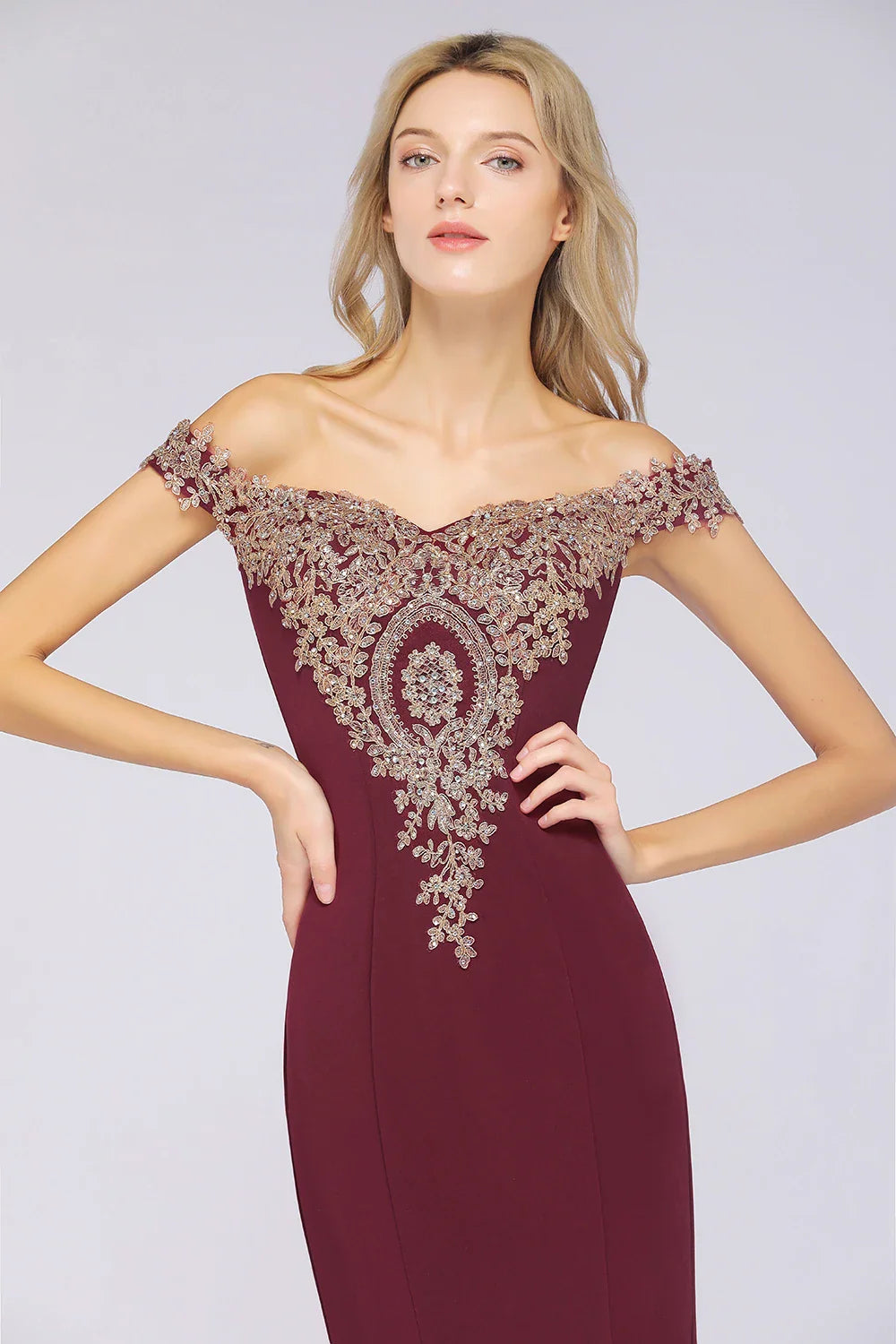 Close up front view of a burgundy off-shoulder mermaid dress with gold appliqué