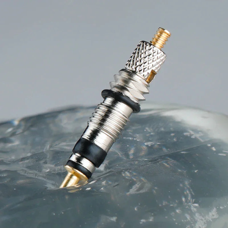 A single brass presta valve core standing upright on a clear surface