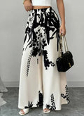 Woman wearing black and white floral print wide leg trousers with a white crop top and black handbag