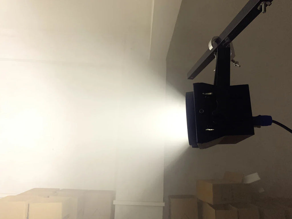Black stage blinder light emitting a bright white wash beam in a dark room