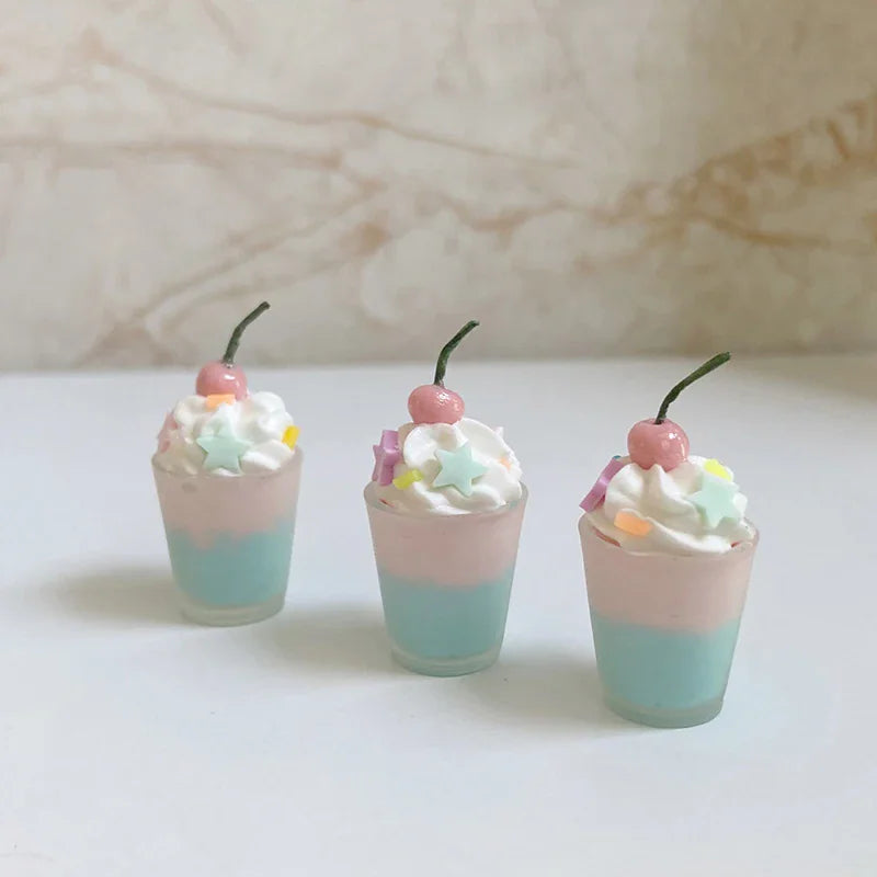 Three miniature dessert cups featuring pink and blue layers topped with whipped cream, star sprinkles, and a cherry.