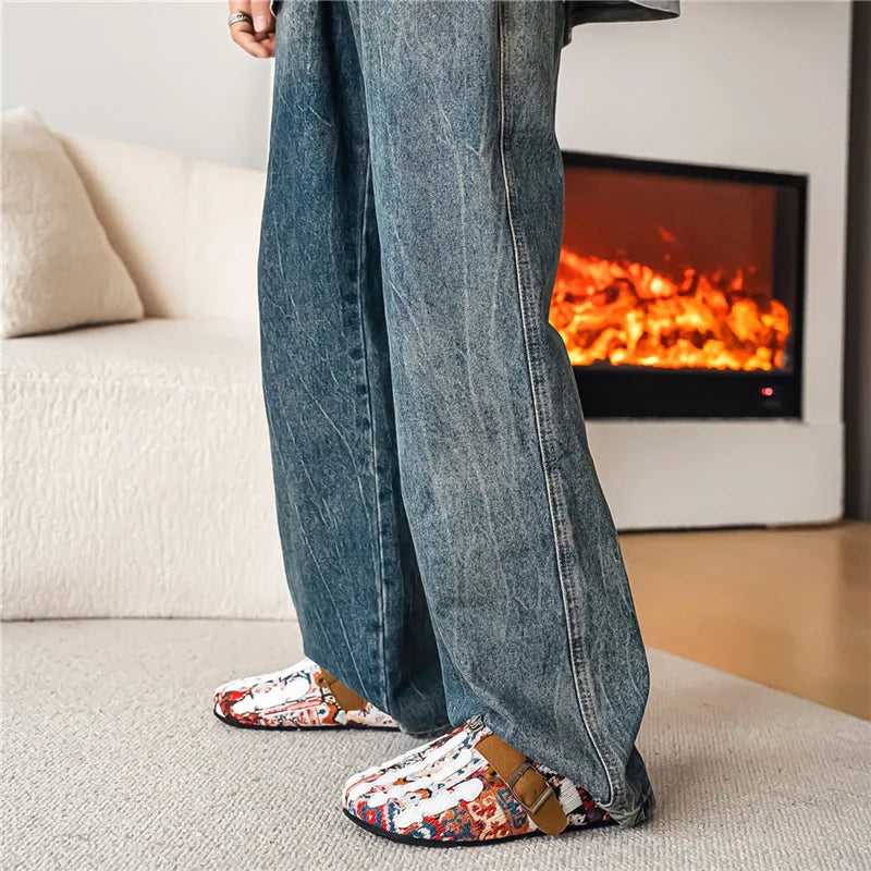 Close up of feet wearing colorful patterned slip-on mule shoes with white skeleton hand design, styled with jeans