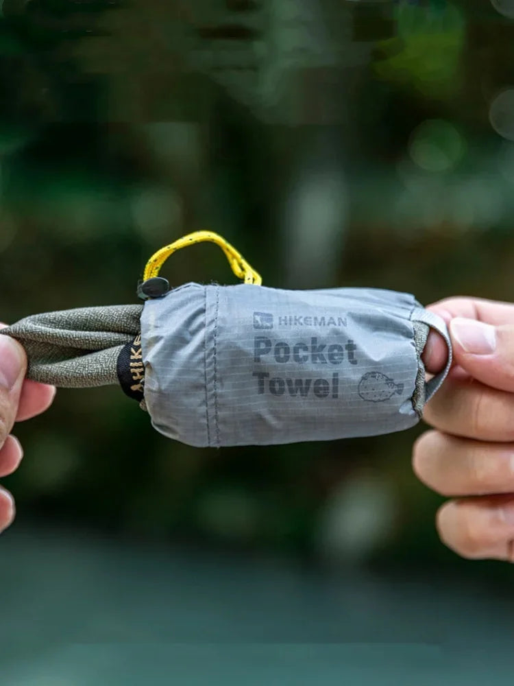Hands holding a grey folded pocket towel with a yellow carabiner.