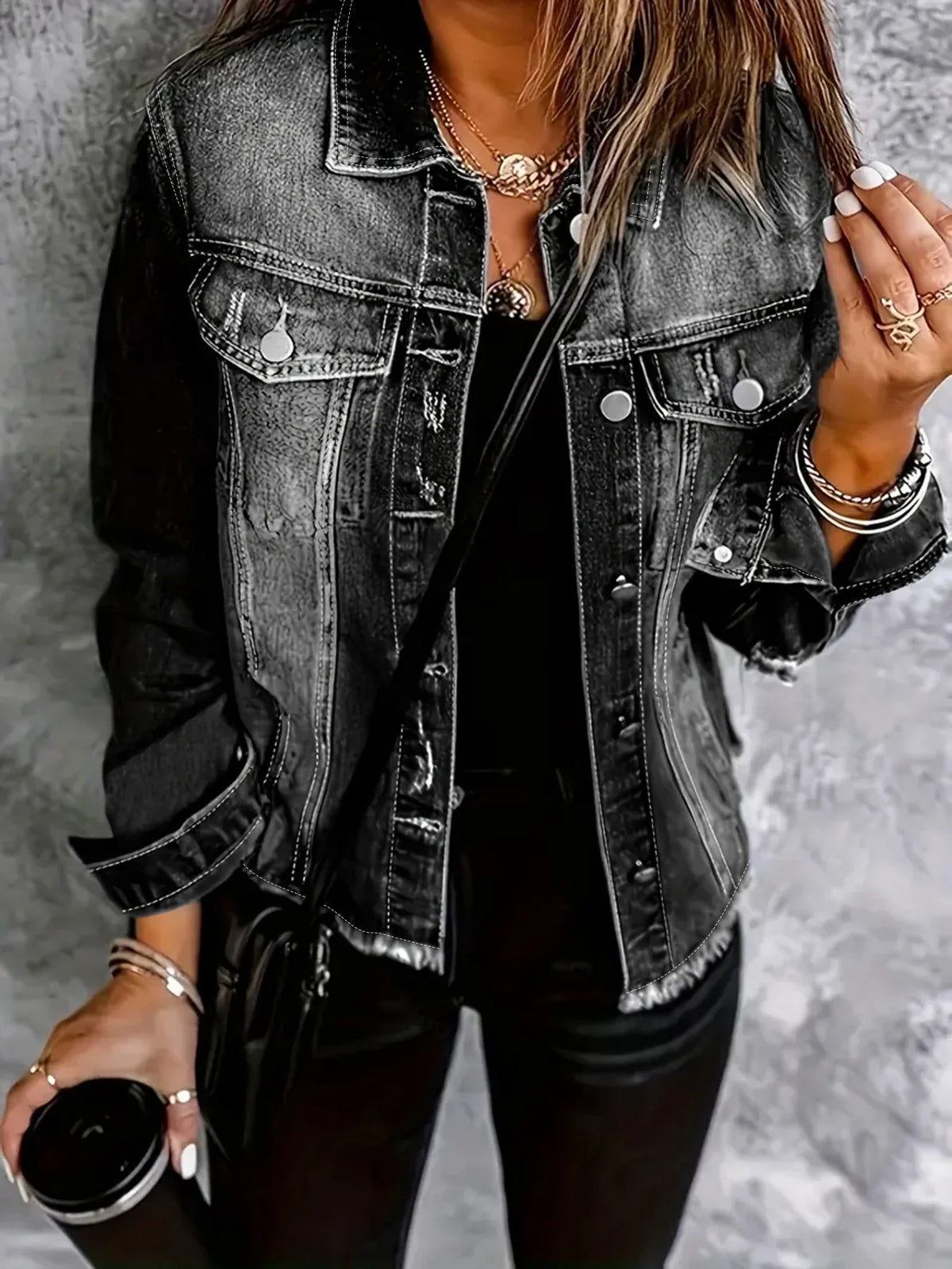 Close-up of a person wearing a dark grey distressed denim jacket, holding a black mug