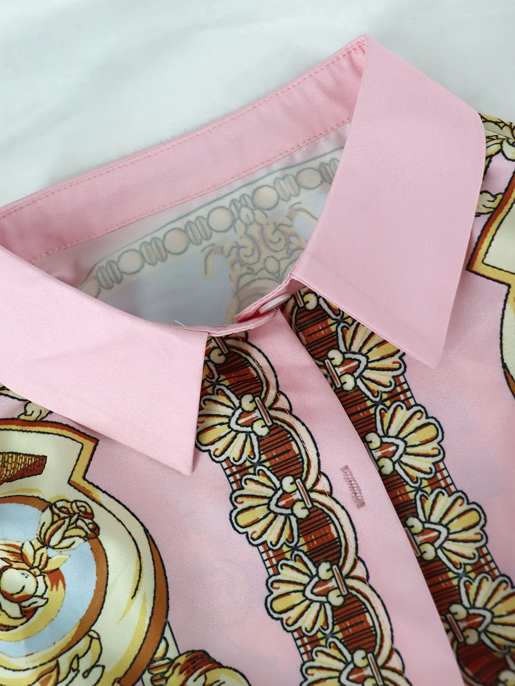 Close up of the pink collared neckline of a women's button-down shirt with gold ornate detailing.