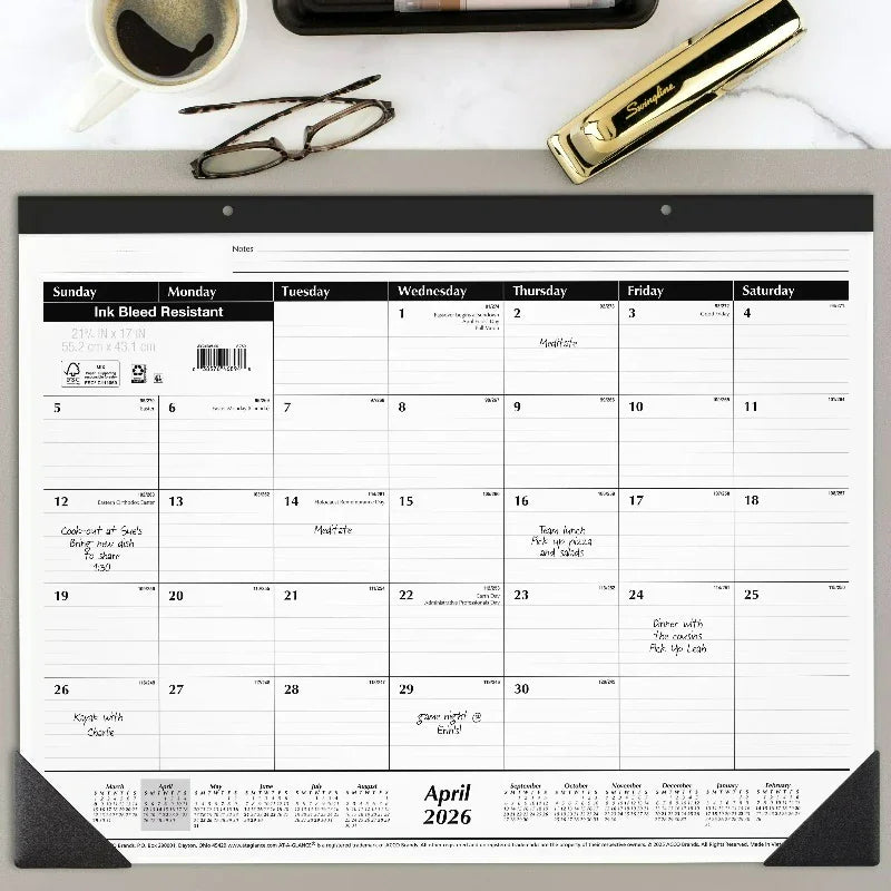 Large paper monthly desk pad calendar for April 2026 on a desk with glasses and stapler