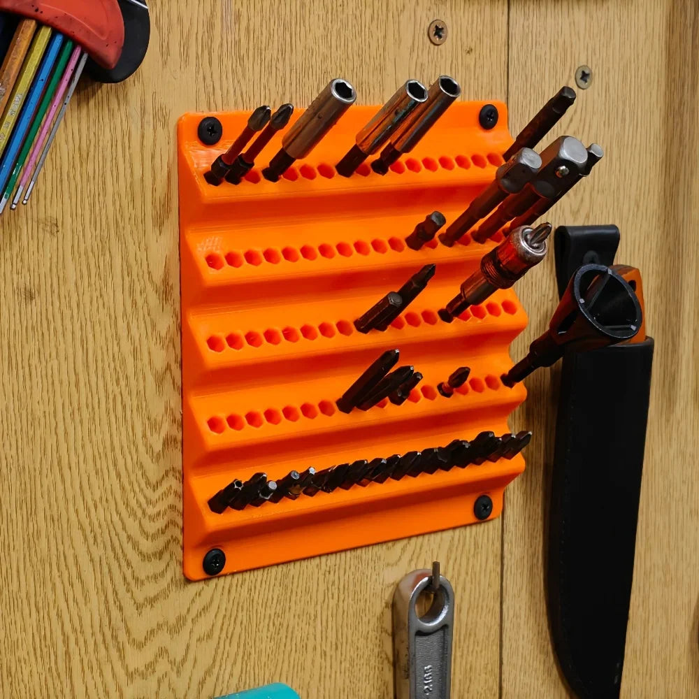Orange wall-mounted organizer rack holding various screwdriver bits and drill bits on a wooden workshop wall.