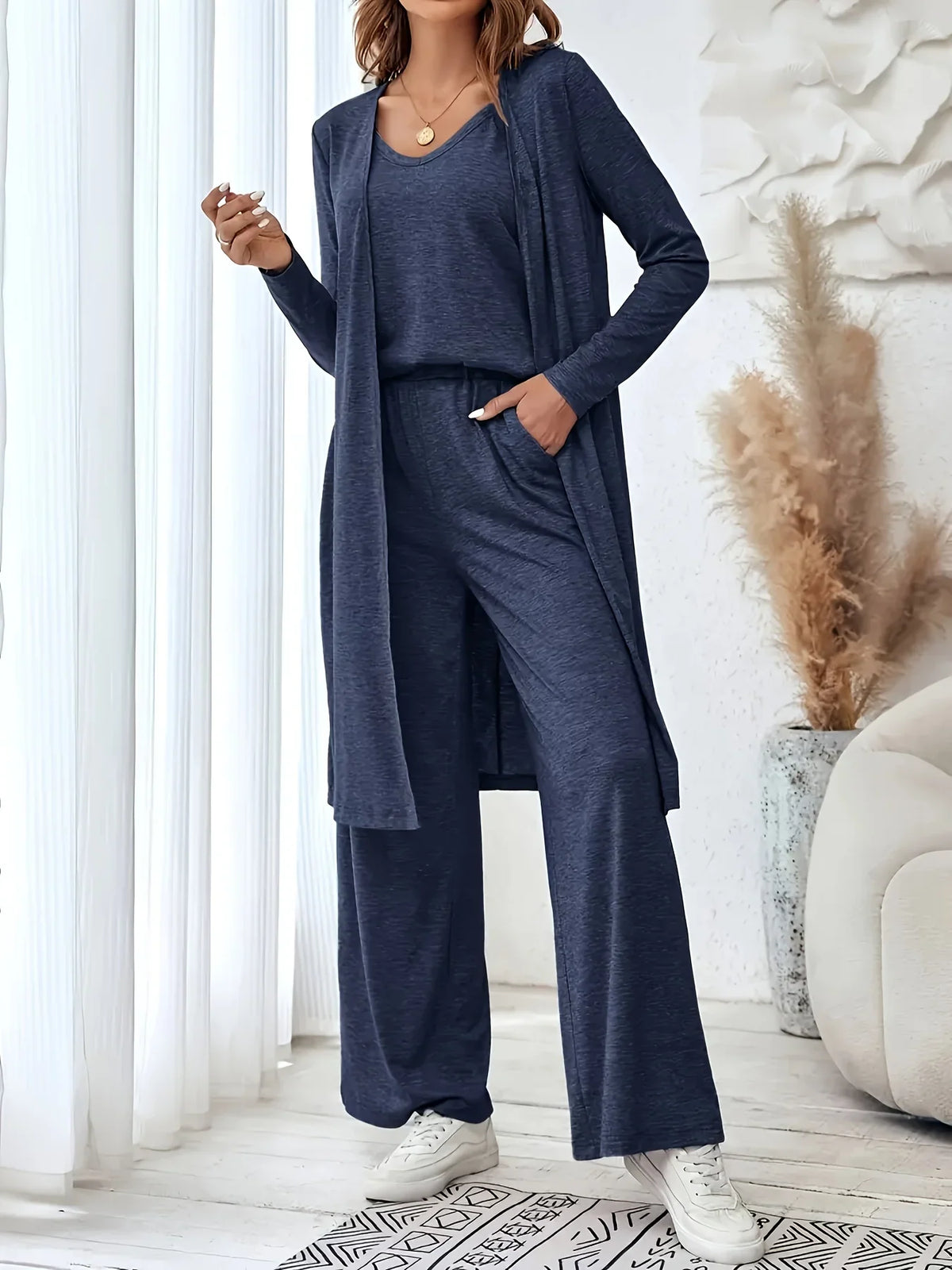A woman wearing a dark blue three-piece loungewear set consisting of a long-sleeve open cardigan, tank top, and wide-leg