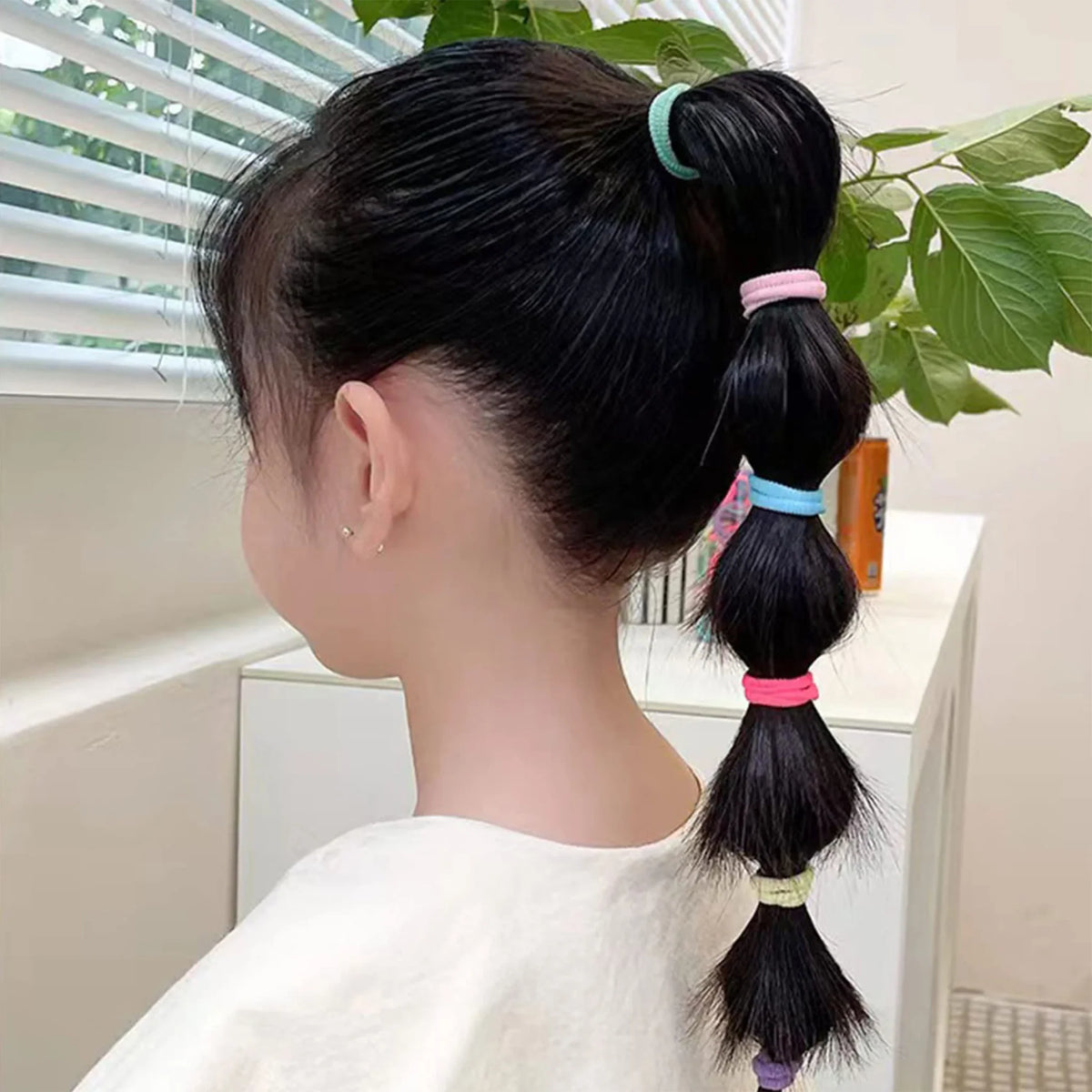 Side view of a girl's ponytail secured in multiple sections by small colorful seamless hair elastics