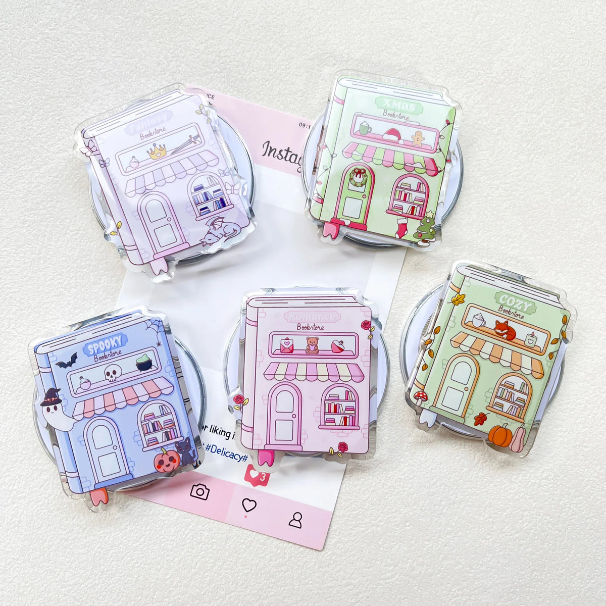 Four assorted acrylic bookstore-themed phone grips arranged on a background with social media branding.