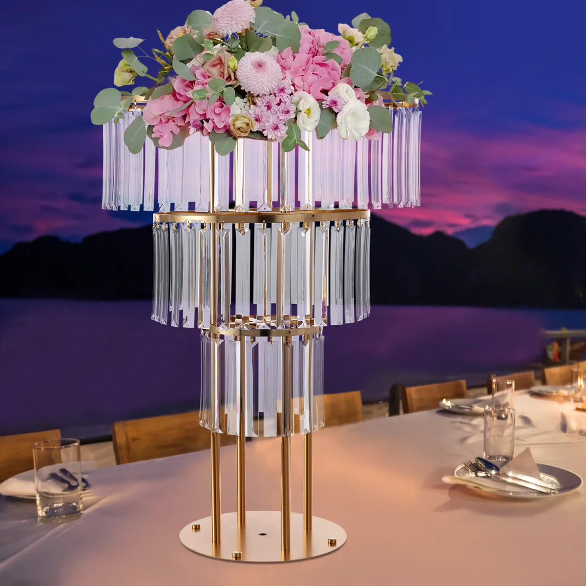 Three-tier gold crystal wedding stand set on a banquet table with a floral arrangement.
