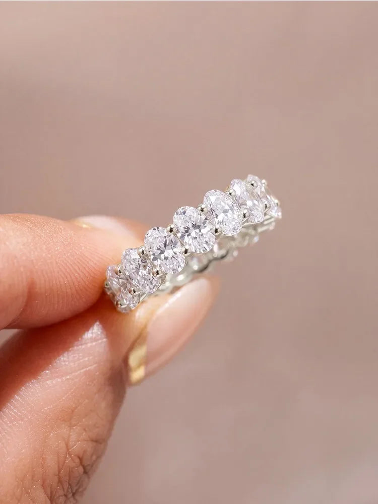 Eternity band ring featuring oval-cut white zircon stones set in sterling silver, worn on a finger.