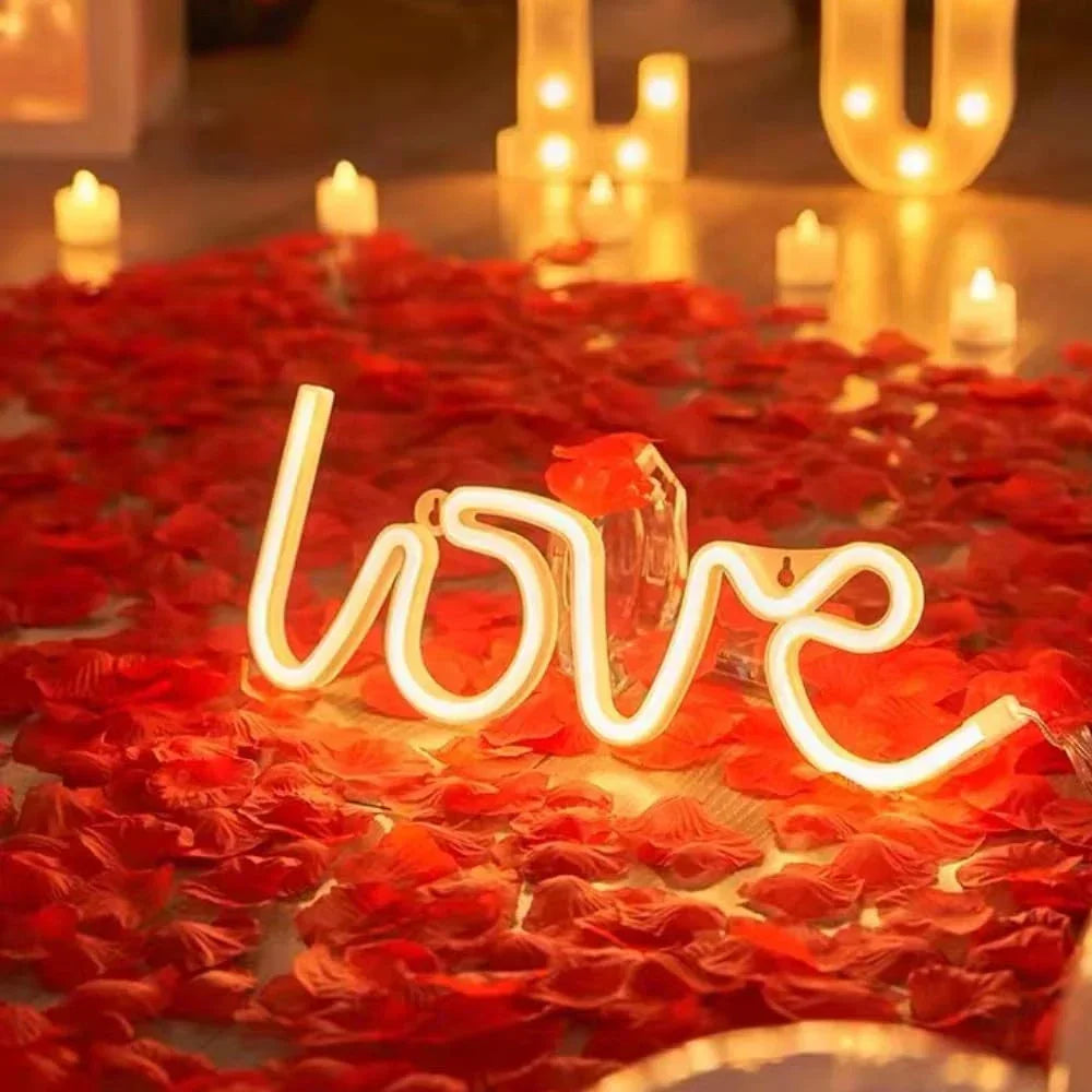 A neon light sign reading LOVE placed on a floor scattered with artificial red rose petals.
