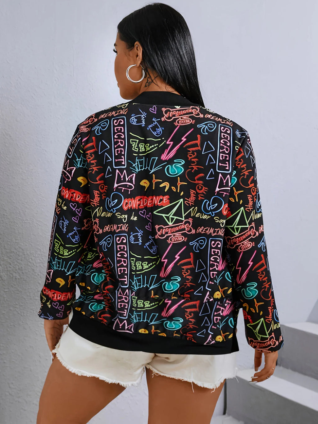 Back view of a plus size woman wearing a black bomber jacket with all-over neon graffiti print.