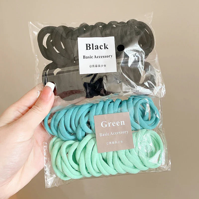 Hand holding a transparent plastic bag containing black and green nylon hair ties with labels.
