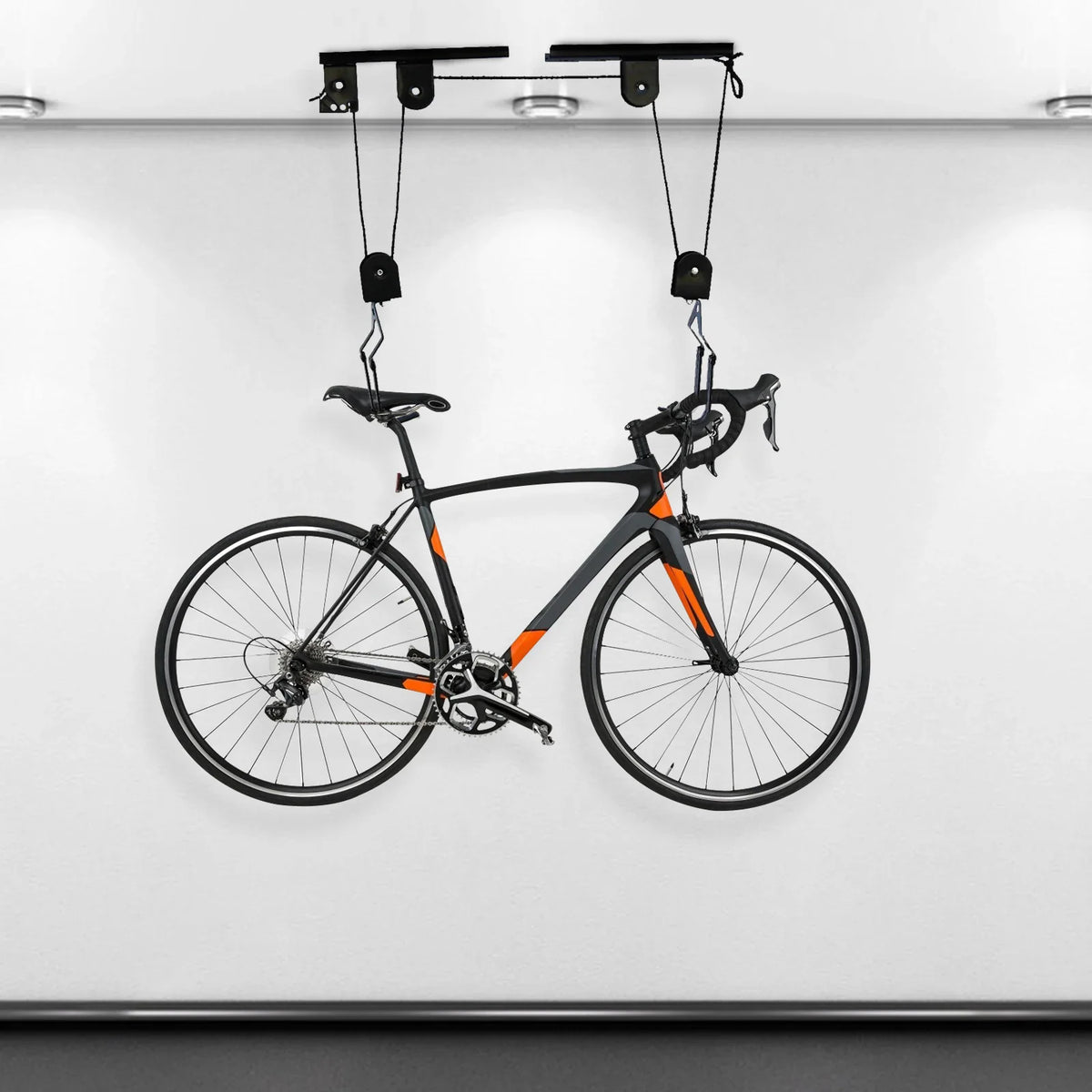 A black road bike suspended from a ceiling by a black pulley hoist system inside a garage.