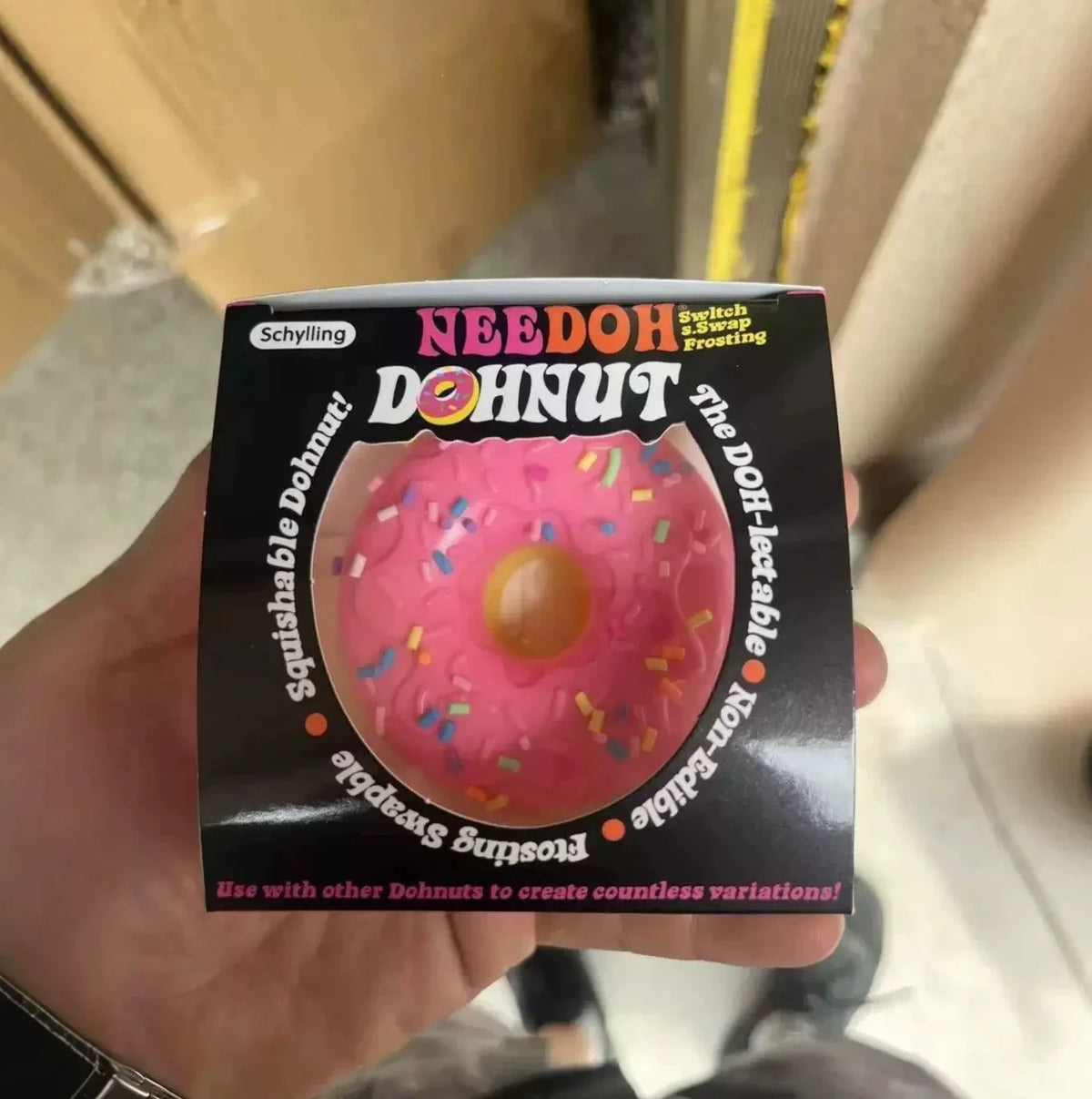 A hand holding a pink squishy donut toy inside its packaging box.