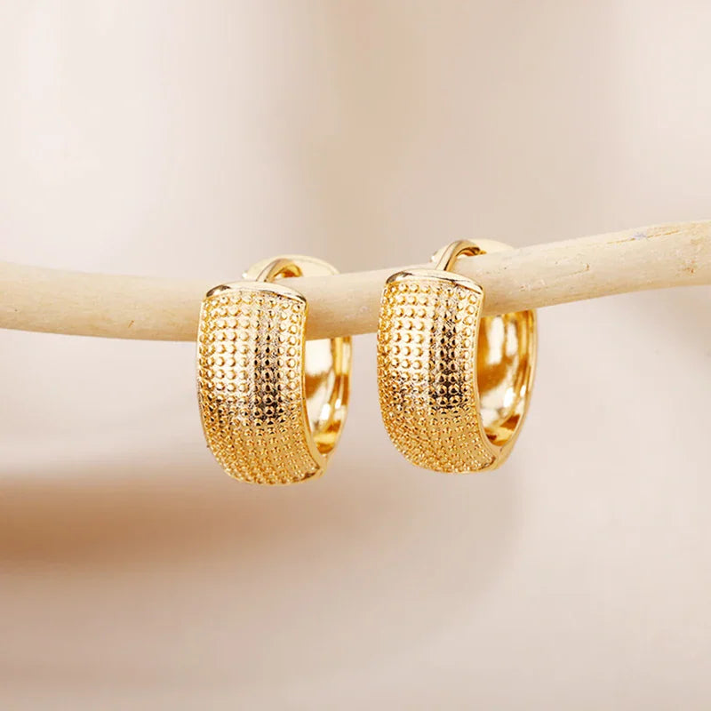 Pair of gold-toned textured huggie hoop earrings hanging on a thin branch