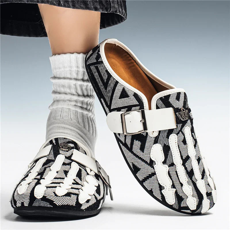 Men's black and white patterned slip-on mule shoes with skeleton hand detail, worn with white socks