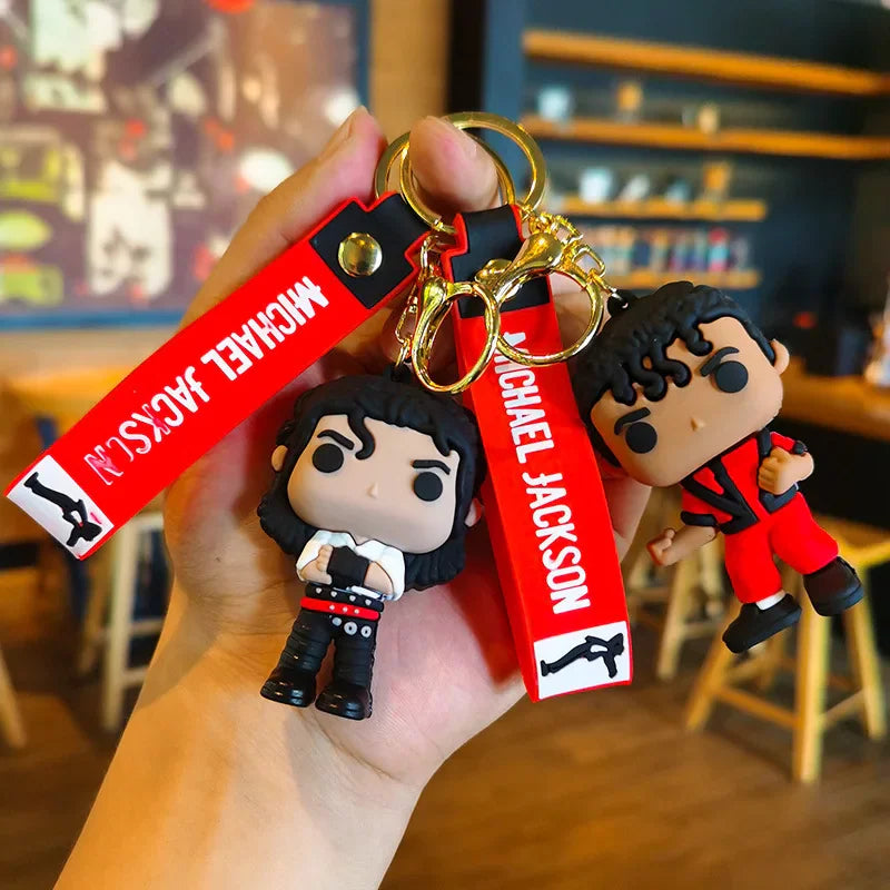 Hand holding two Michael Jackson vinyl-style doll keychains, one in black and white, one in a red suit.