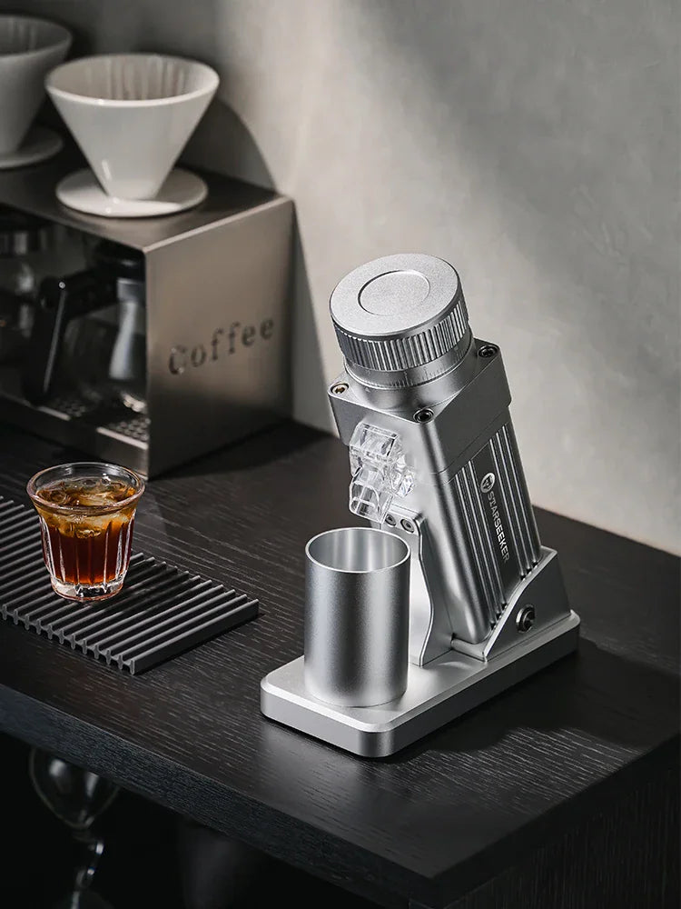 Silver electric coffee grinder placed on a dark table next to coffee brewing equipment