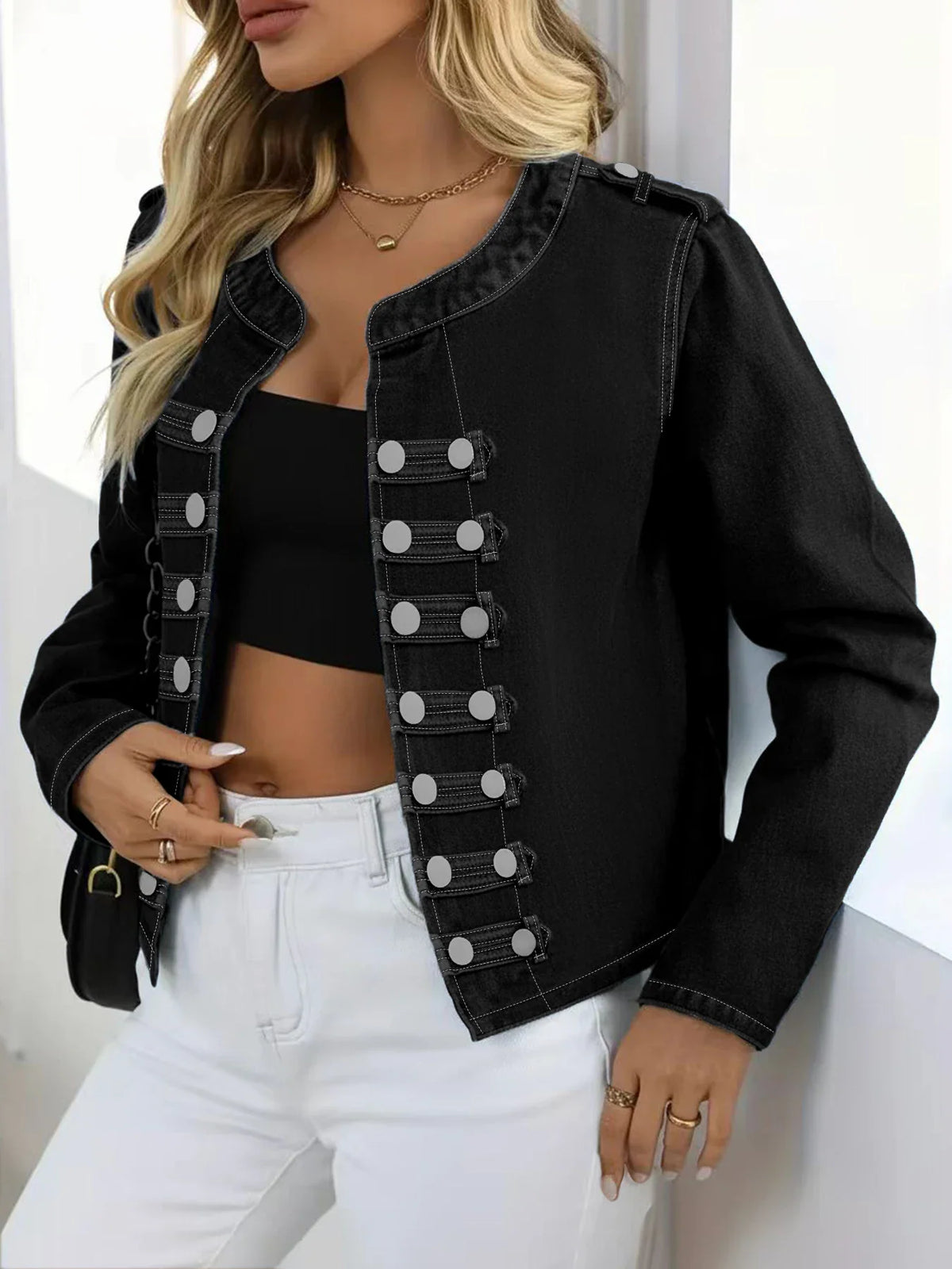 Side view of a woman wearing a black washed denim jacket with silver buttons and white jeans