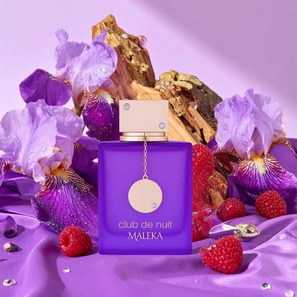 A vibrant purple glass perfume bottle placed amongst fresh raspberries and purple flowers.
