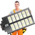 A man in work clothes holding a large solar LED street light.