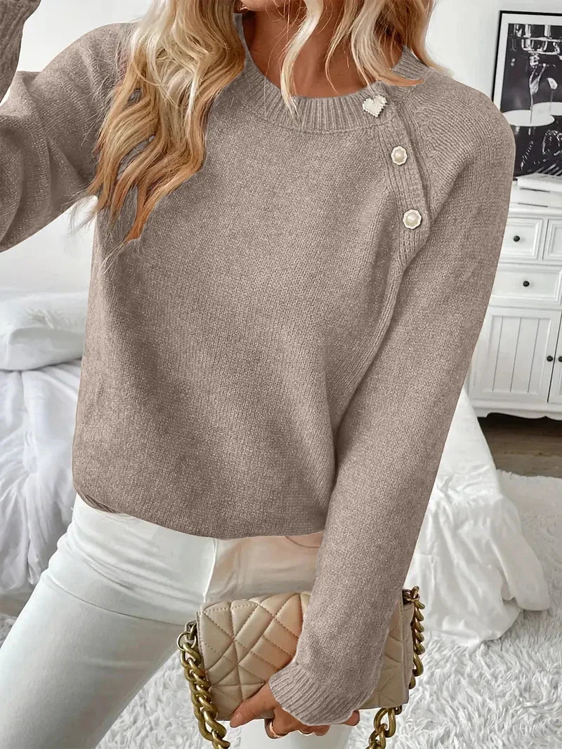 A woman wearing a solid color long-sleeve knit sweater with decorative gold buttons on the shoulder.