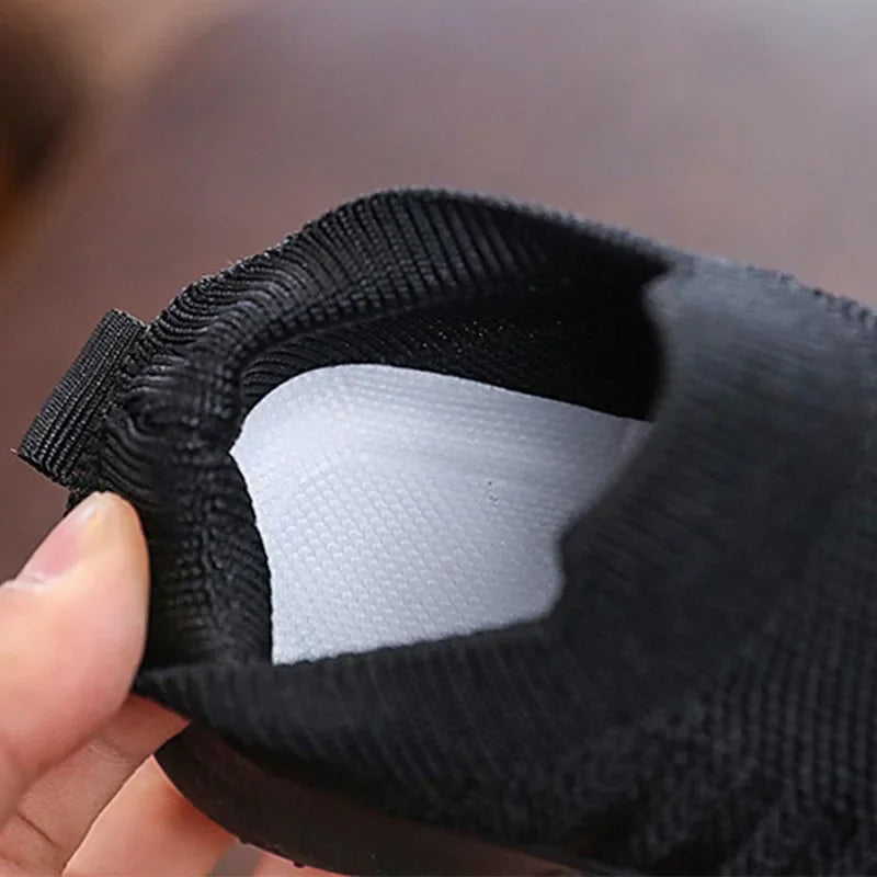 Close up of the interior of a black kids knitted slip-on sneaker held by a hand