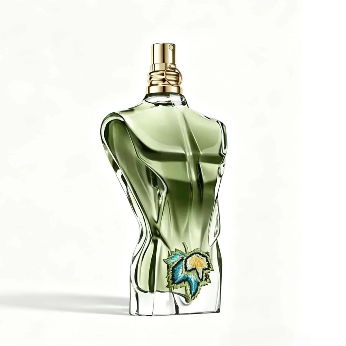 Green glass perfume bottle shaped like a male torso with a tropical leaf embroidery on a white background