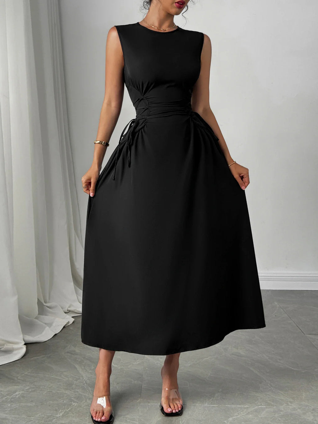 A woman wearing a black sleeveless midi dress with a fitted waist and flared skirt.