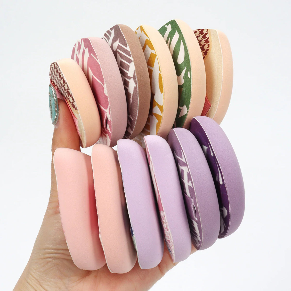 A hand holding a selection of various colorful makeup puffs in different patterns