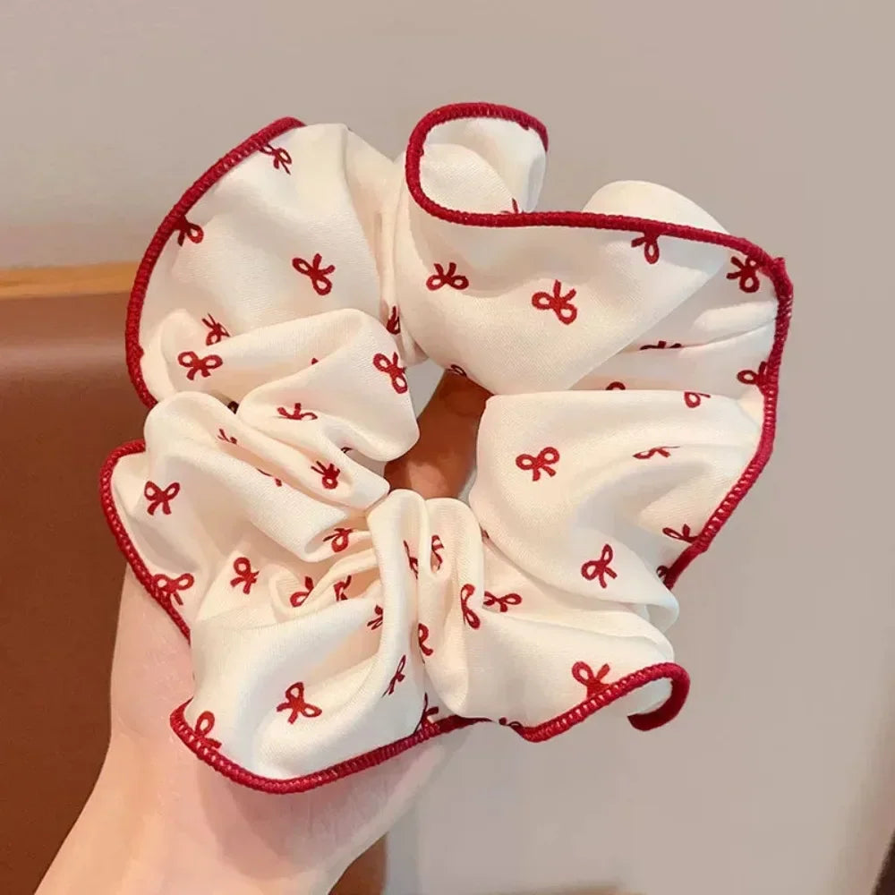 A white hair scrunchie with small red bows and a ruffled red trim being held in a hand