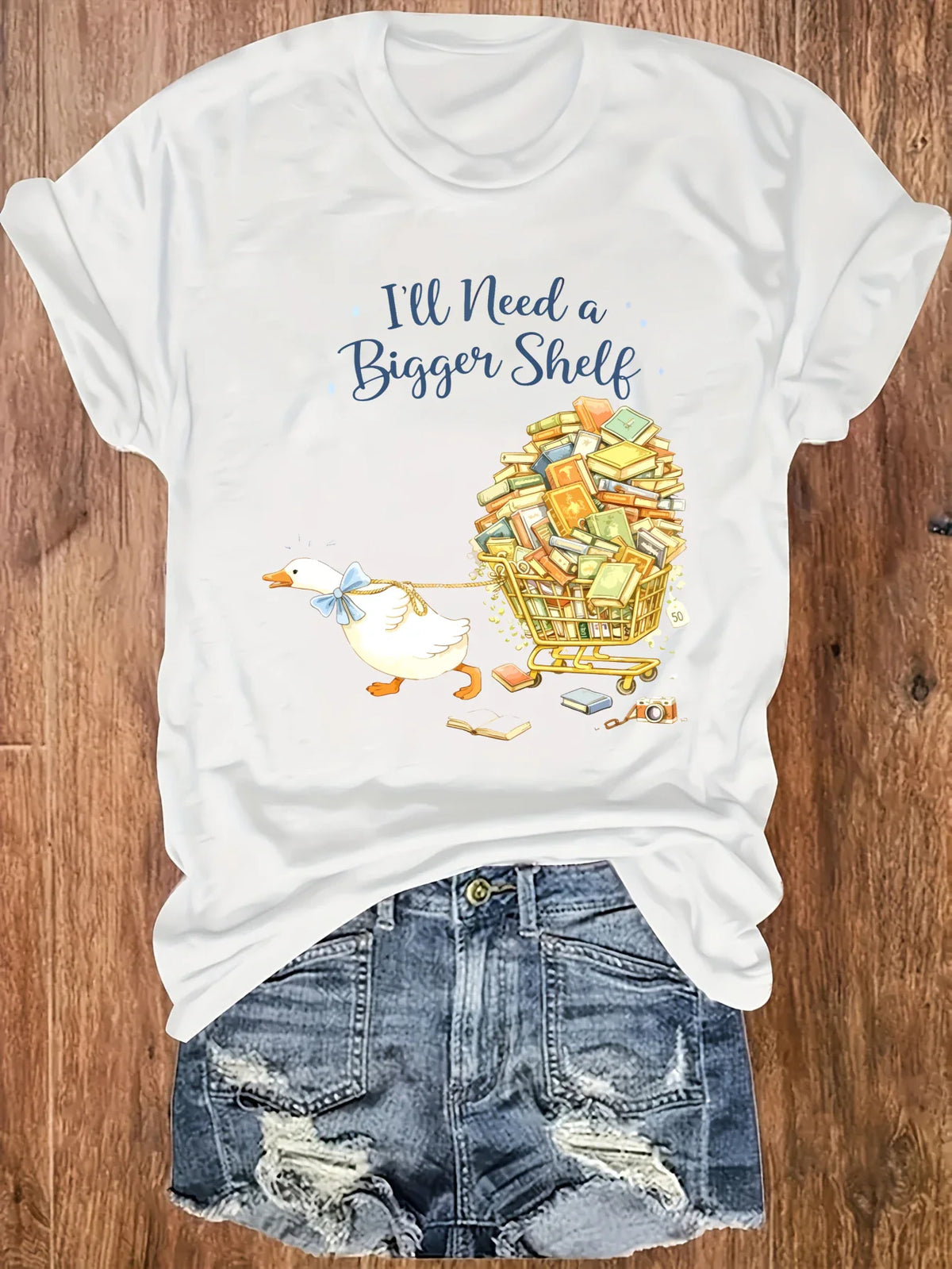 White short-sleeved t-shirt with a duck pulling a book cart graphic print, styled with denim shorts