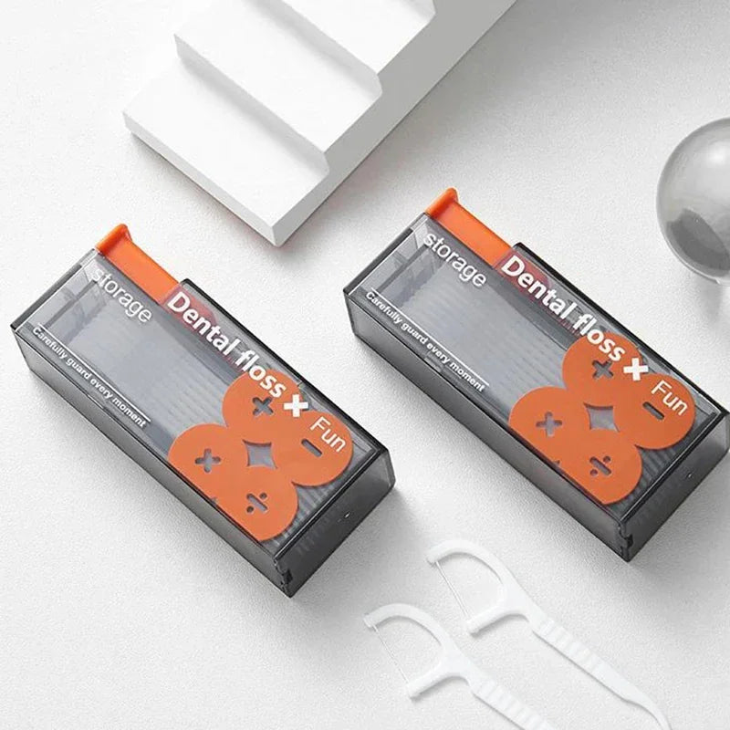 Two portable dental floss dispensers in grey and orange, displayed next to individual white plastic dental floss sticks.