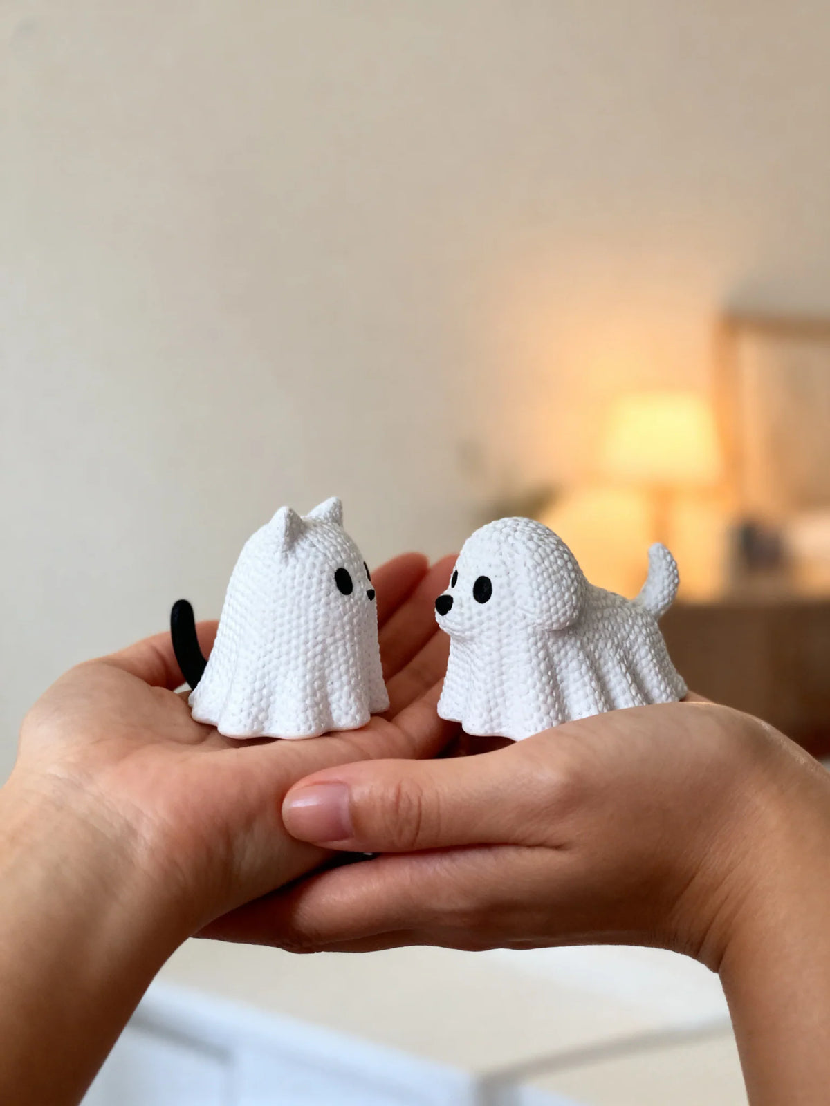 Set of two small white ghost-themed cat and dog decorative figurines held in hands