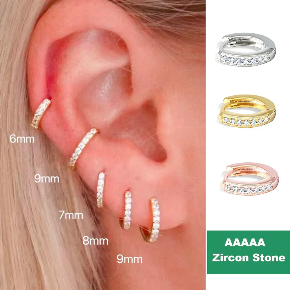 Set of gold, silver and rose gold small hoop earrings with cubic zirconia crystals worn on an ear.
