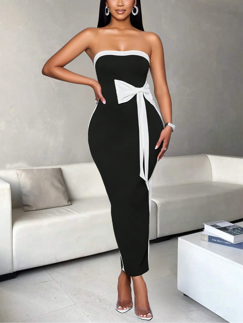Woman standing and wearing a fitted black and white strapless dress with side bow