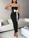 Woman standing and wearing a fitted black and white strapless dress with side bow