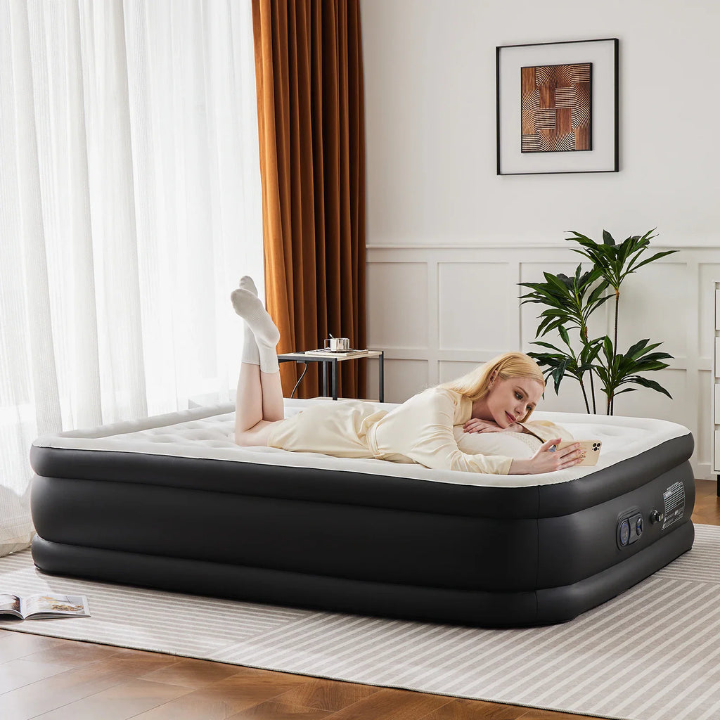 A woman lying on a queen-sized black and white air mattress in a bedroom.