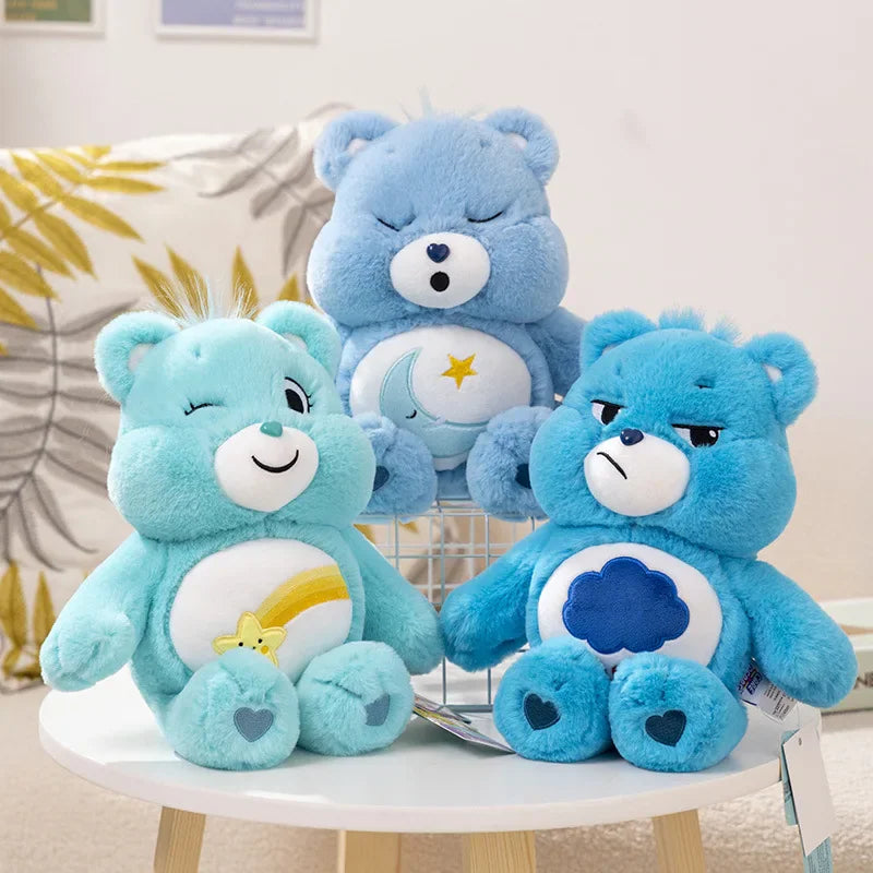 Three blue Care Bear plush toys with different belly badge designs sitting on a white table
