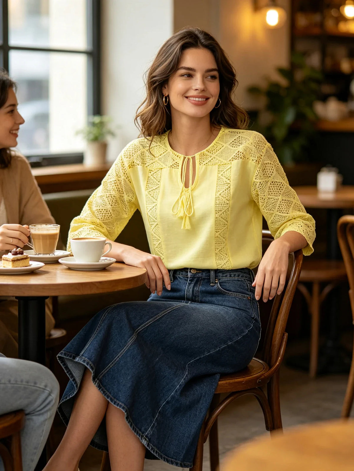 Woman wearing a yellow lace-stitched blouse and a dark denim midi skirt in a cafe