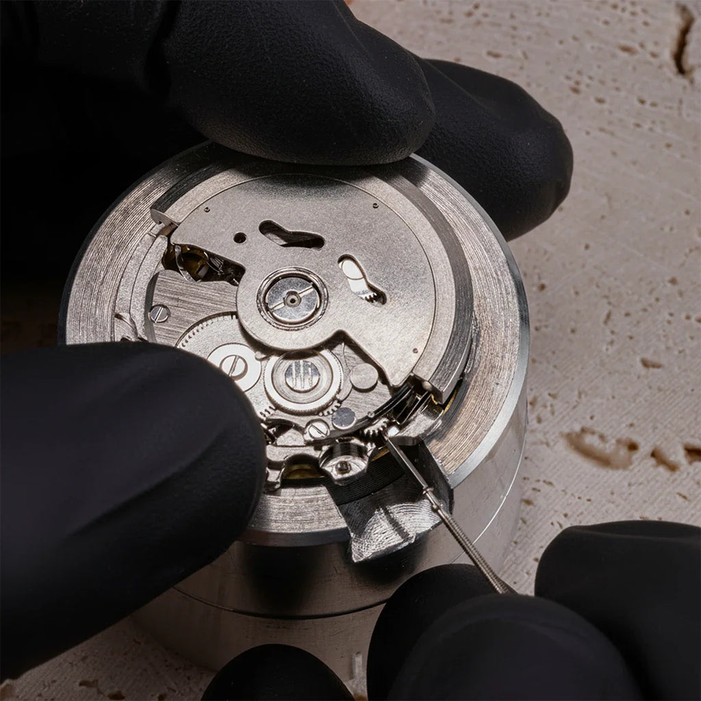 Gloved hands working on an automatic mechanical watch movement