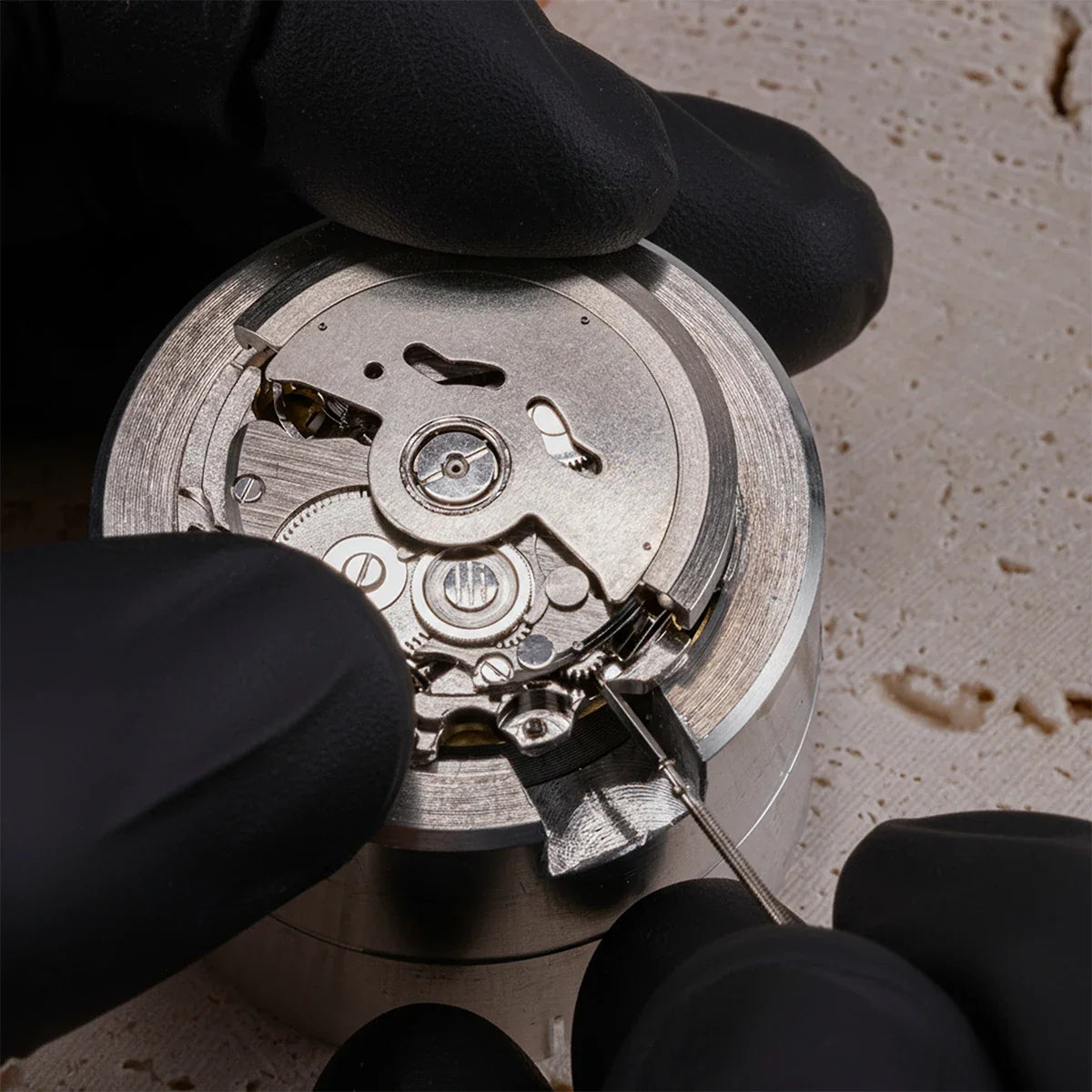 Gloved hands working on an automatic mechanical watch movement