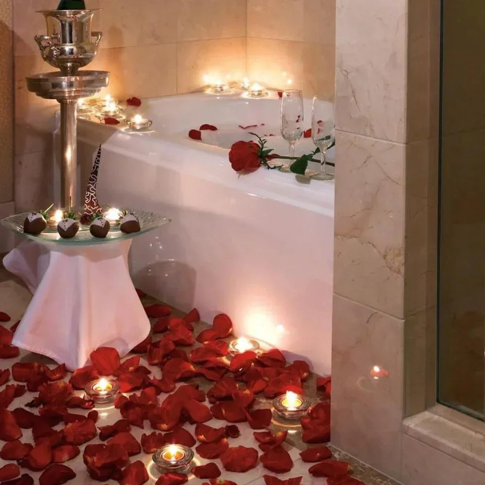 Romantic bathtub decoration with tea light candles and scattered artificial red rose petals.