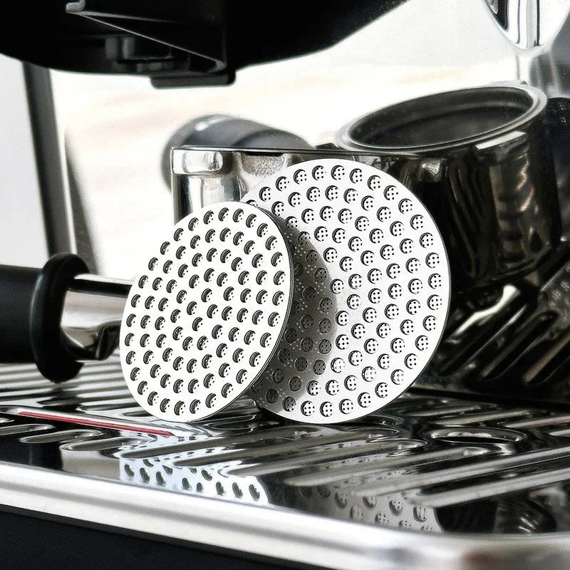 Two stainless steel espresso puck screens of different sizes resting on an espresso machine drip tray
