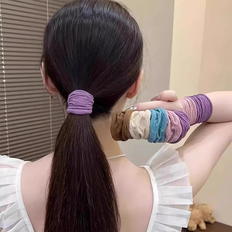A woman with a ponytail secured by a purple hair scrunchie, holding a collection of other colorful scrunchies