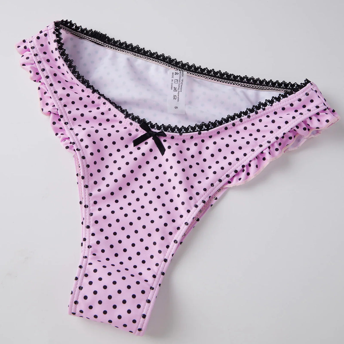 Pink polka dot thong bikini bottom with black lace trim and small black bow.