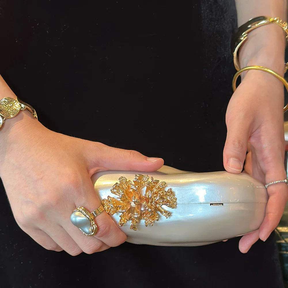 White marbled acrylic evening clutch with gold coral-shaped clasp held by a woman